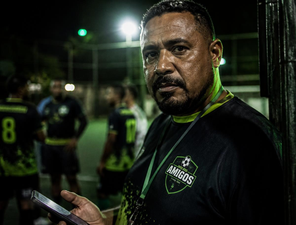 Organizador de pelada com o celular na mão à beira da quadra iluminada
